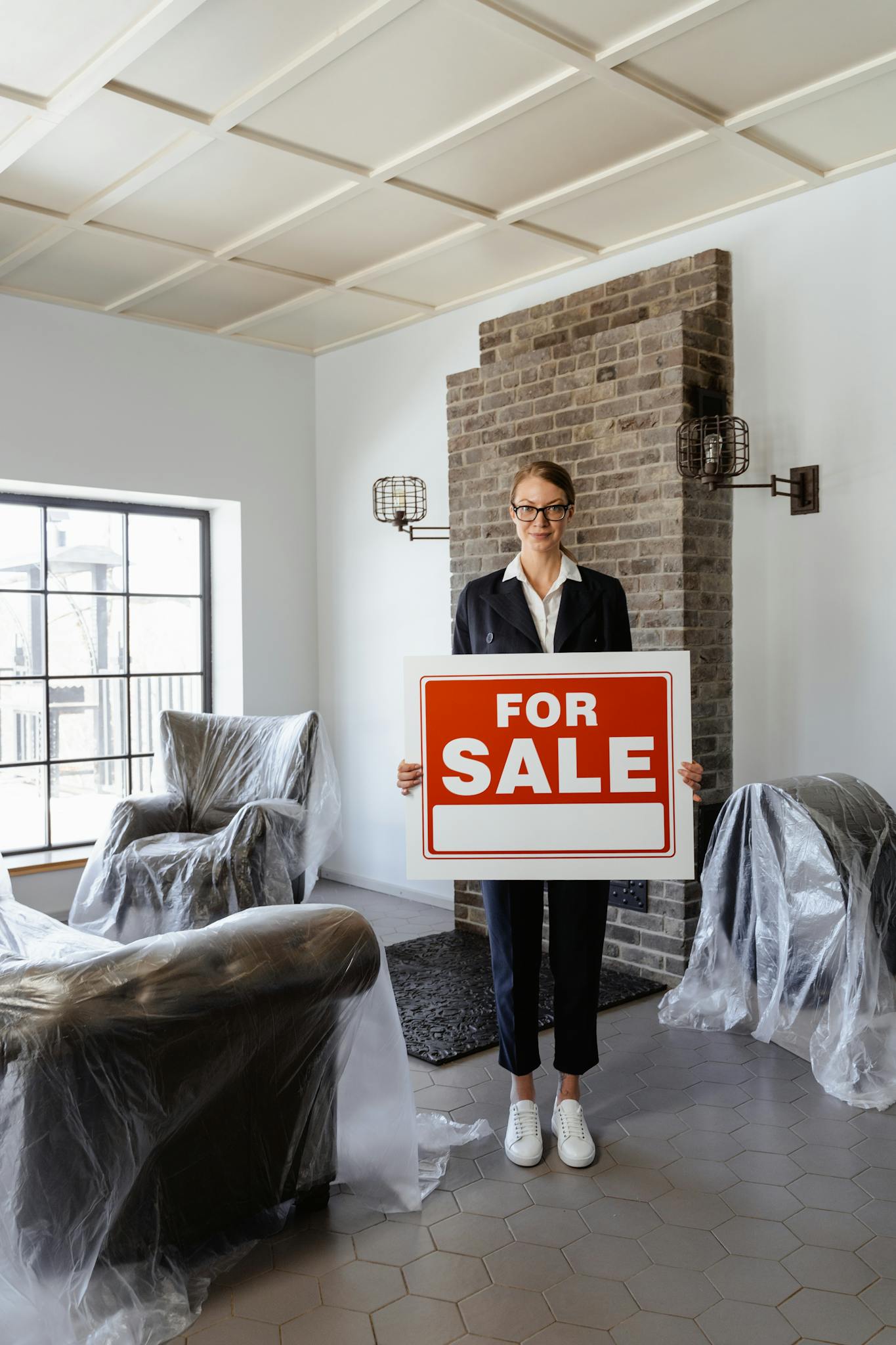 Professional real estate agent holding a 'For Sale' sign in a furnished indoor setting.